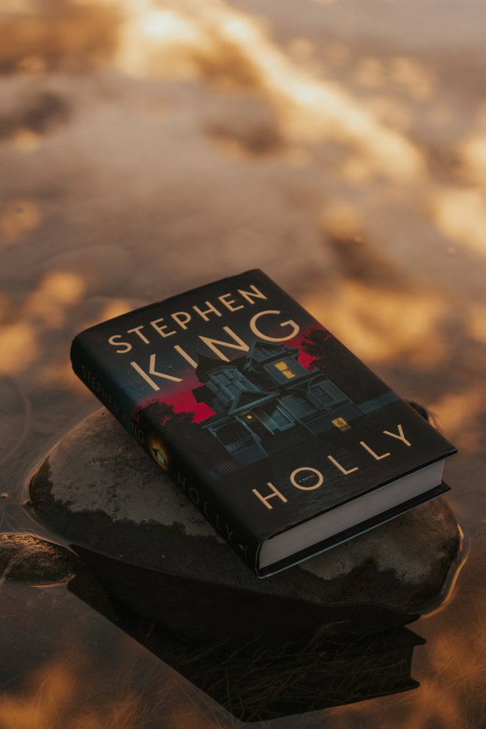 A copy of the book Holly resting on a black rock in a river. The water's blurred reflection is golden.
