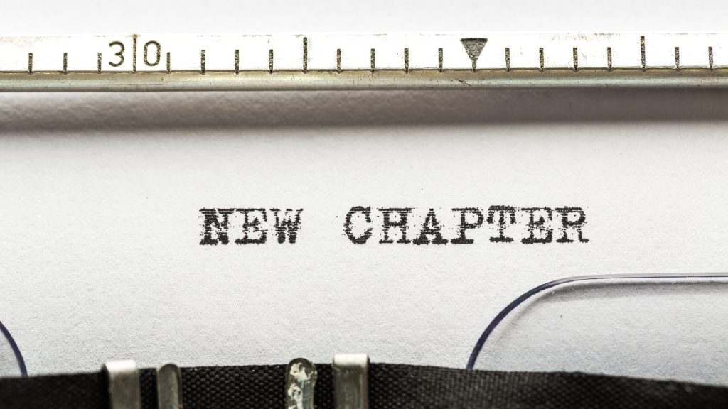 Close up of a paper in a typewriter reading "NEW CHAPTER" in all caps.