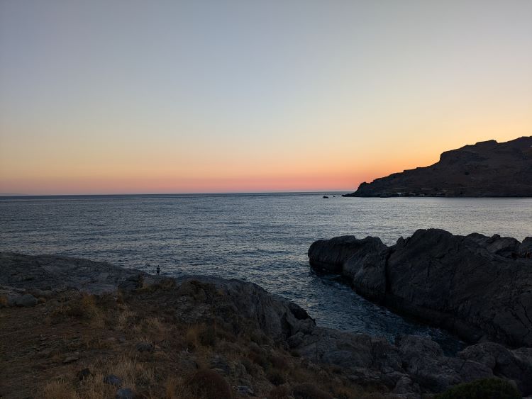 Image of a sunset over an ocean with a rocky coastline jutting out into the water.