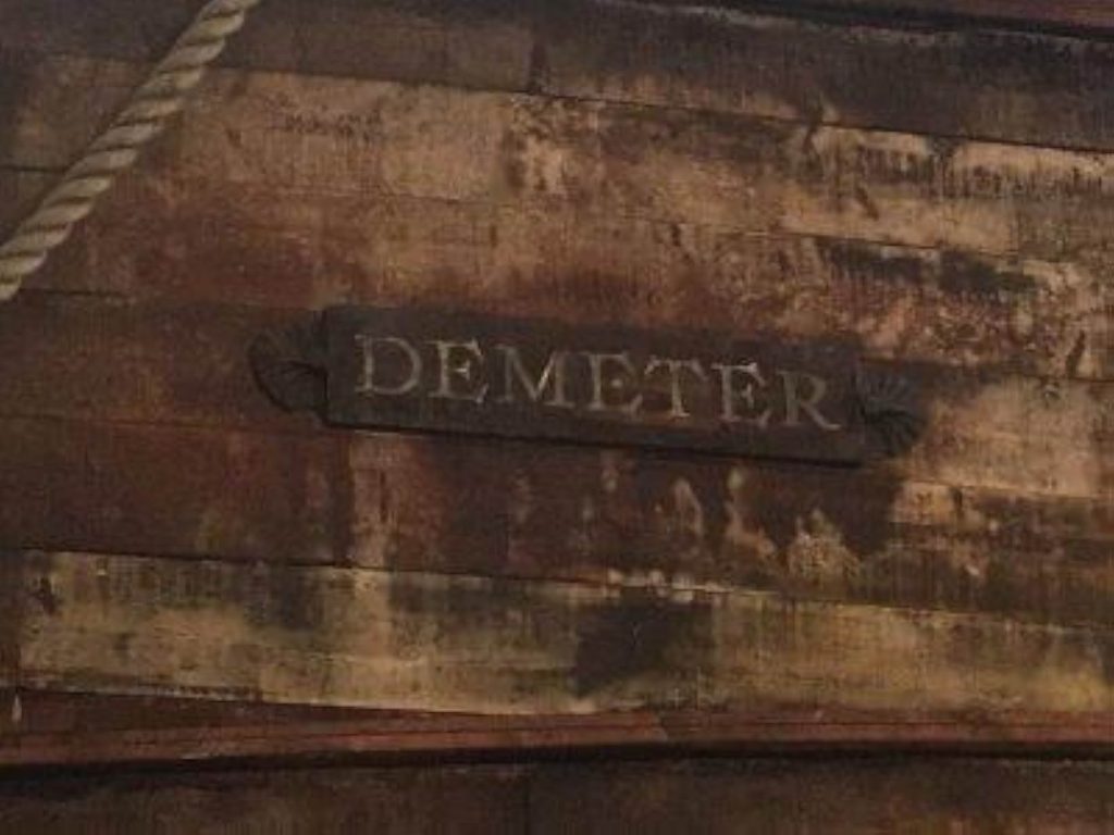 A still from the 2020 mini-series Dracula. The side of a worn wooden ship has a rusted iron placard with DEMETER carved into it.