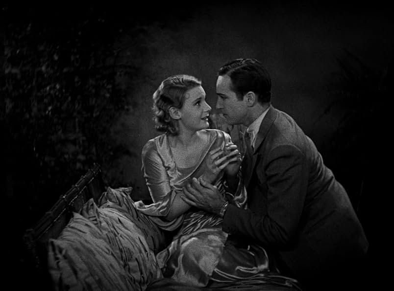 A still from the 1931 movie Dracula. In black and white, a young woman in a pale silk dress sits on a cushioned chaise and looks fearful. A man in a dark suit holds her close and gazes into her eyes with a comforting expression.
