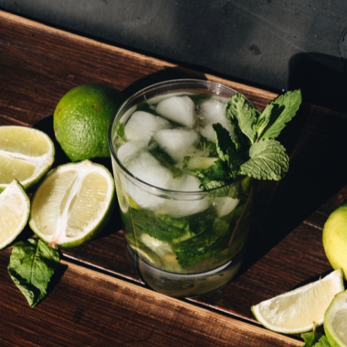 Mint julep in a short clear glass with ice and a mint garnish surrounded by cut limes.