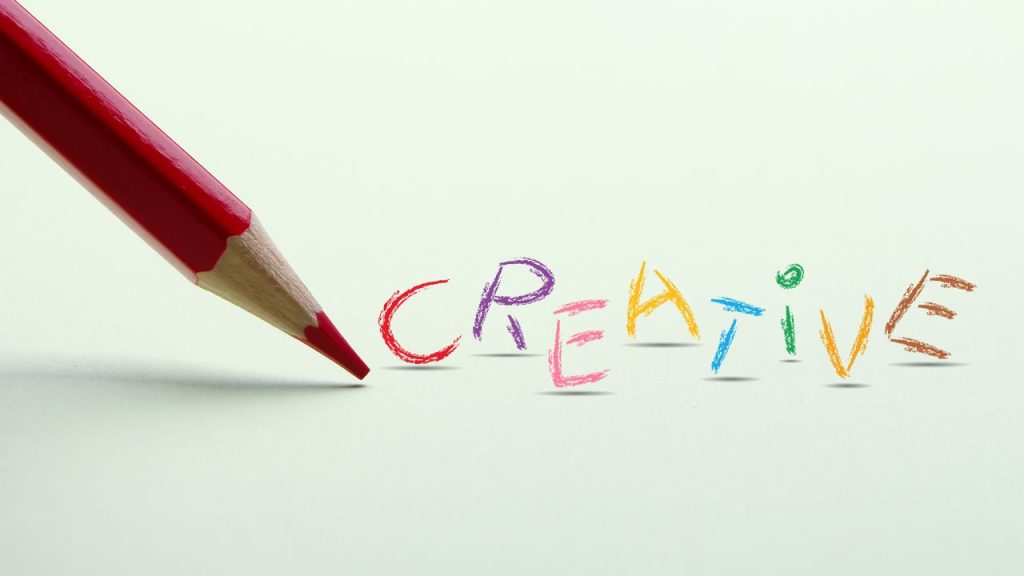 The word "creative" is written in colorful letters with a red colored pencil next to it against a white background.