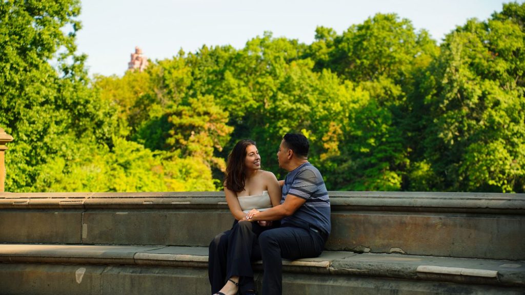 A couple sitting and talking on a stone bench outside.