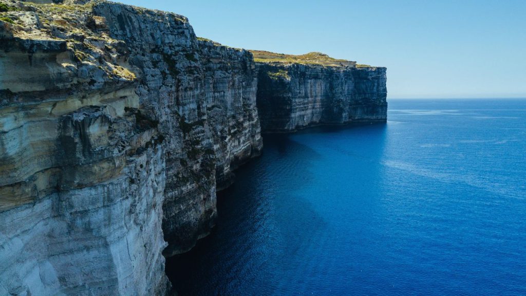 An expansive cliffside with blue water at the base.