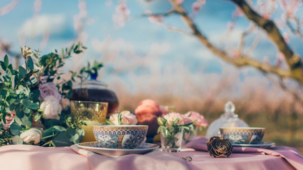 A table with roses, pink table cloth, and tea cups in an outdoor setting.