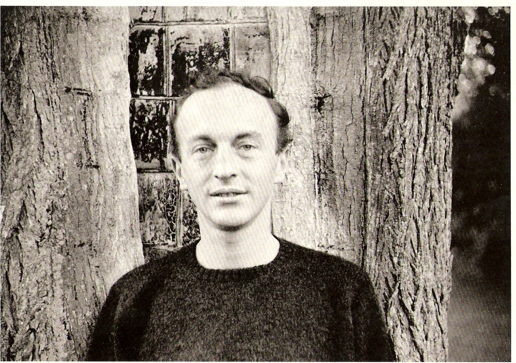 Frank O'Hara stands in front of a tree and smiles while looking into the camera.
