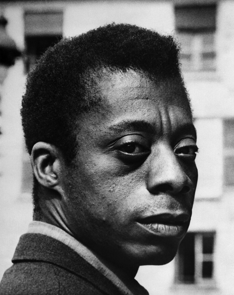 Black and white portrait of James Baldwin looking into the camera.