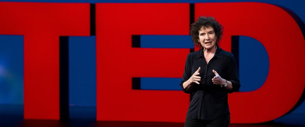 Jeanette Winterson wears a black shirt and speaks in front of a red TED sign.
