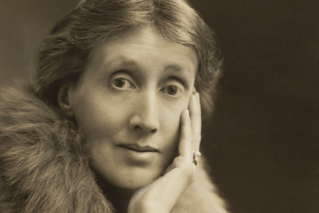 Portrait of Virginia Woolf looking into the camera and wearing a fur coat with her head resting in her hand.