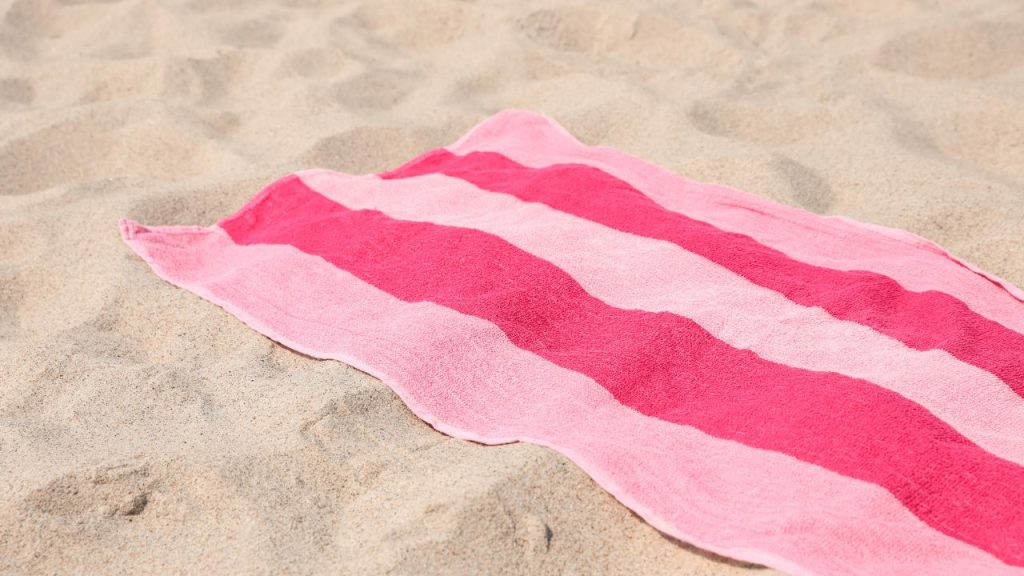 A pink striped beach towel spread out on light sand.