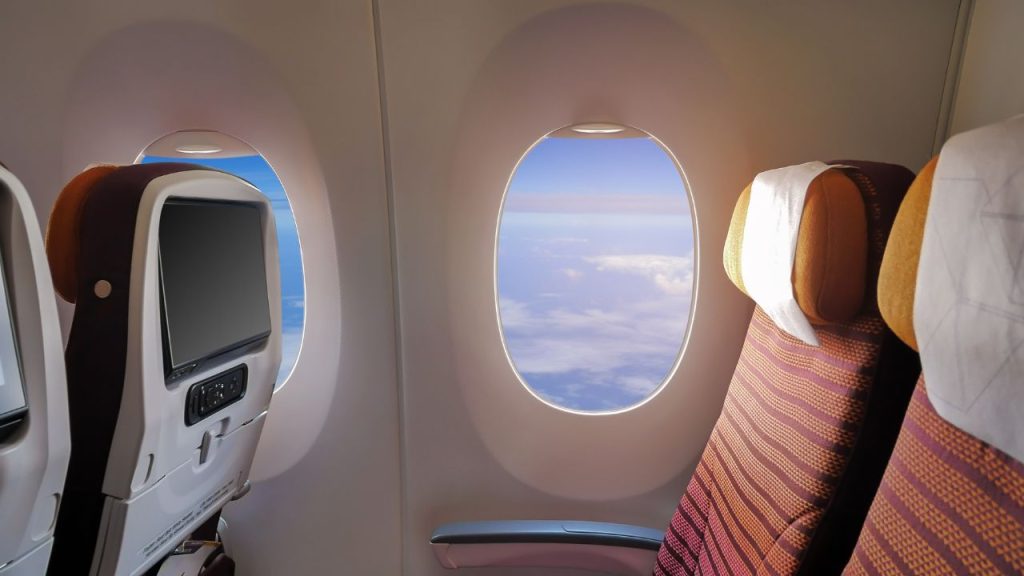 Inside a plane with a window overlooking a blue sky with clouds.