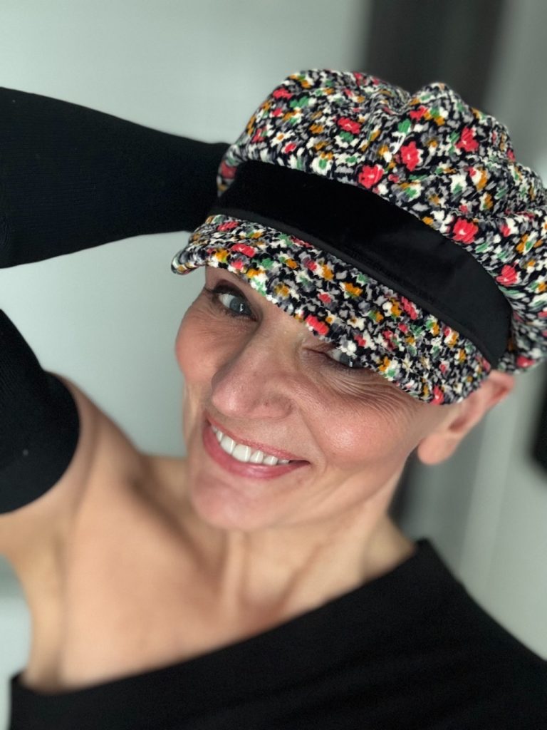 Picture of Tina Martel smiling while wearing a black long-sleeve shirt and a floral hat.