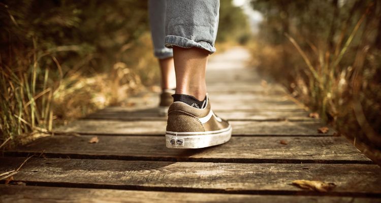 A person's foot shown at the ankle, walking in nature down a wooden path.