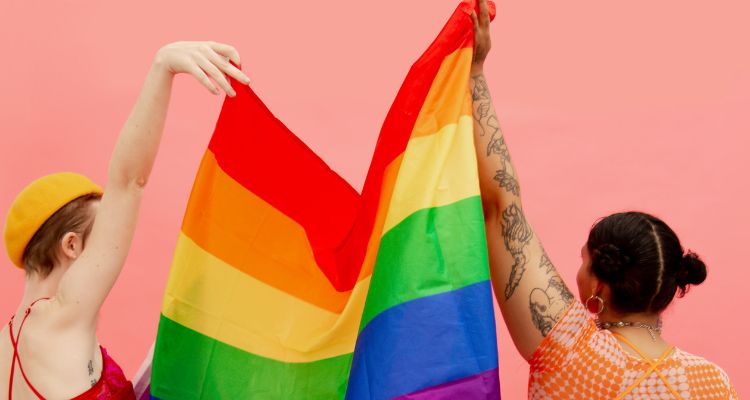 Two people holding up the Pride flag between them on a hot pink background.