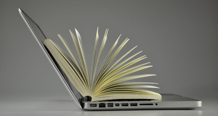An open laptop with a book fanned out onto of it.