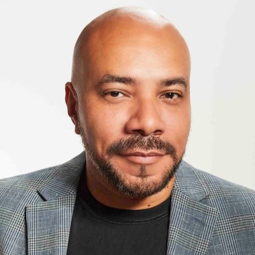 John Jennings, a bald Black man, looks at the camera against a white background.