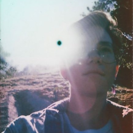 Molly Knox Ostertag poses on a hill with trees, her right eye obscured by a bright glare.