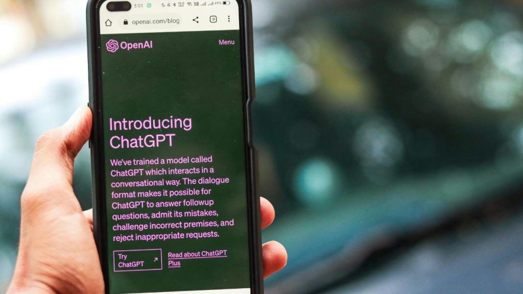 A hand holds a smartphone displaying a webpage titled "Introducing ChatGPT" by OpenAI. The screen text explains the AI's conversational abilities.