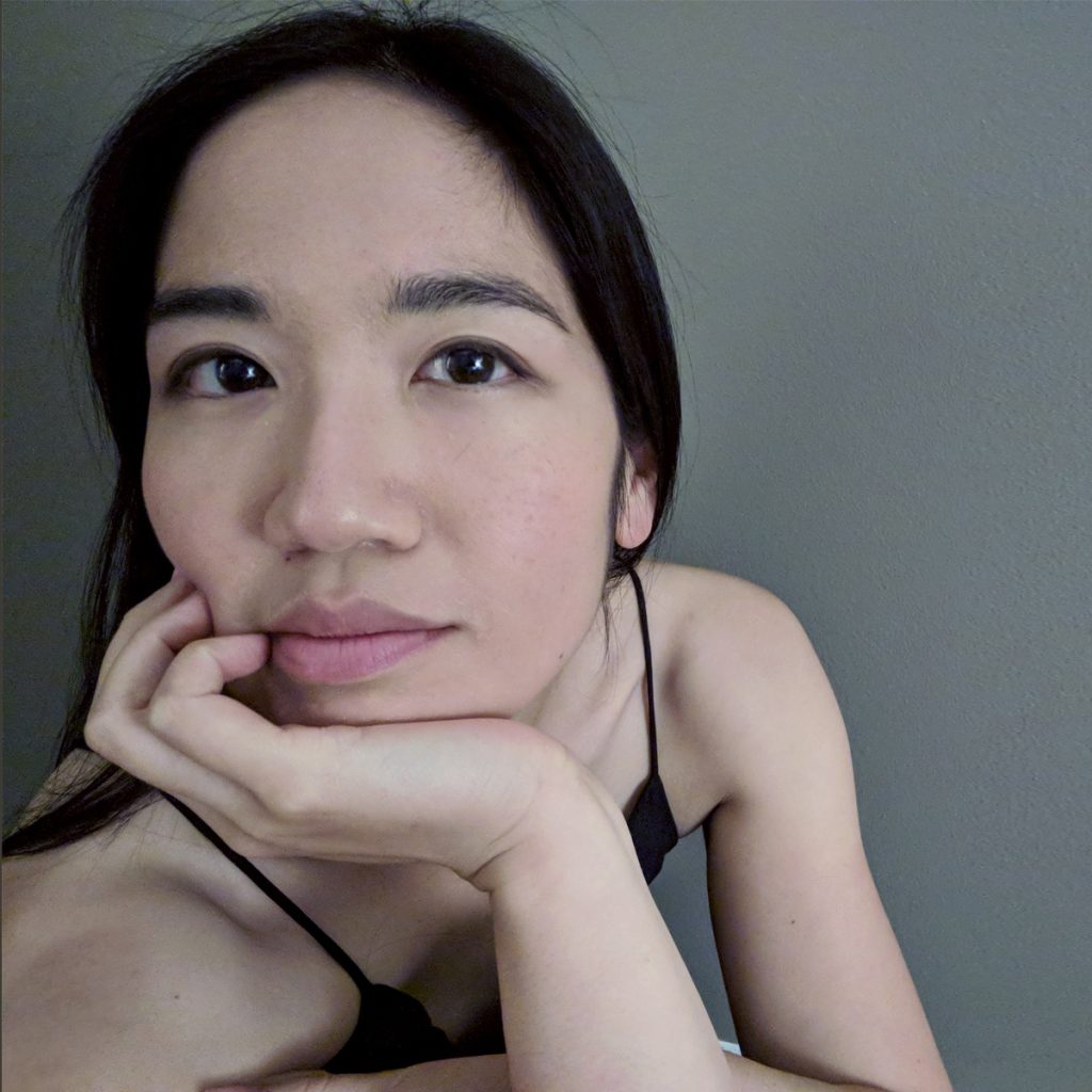 Regina Linke wears a black tank top and rests her chin on her hand. She is in front of a gray background.