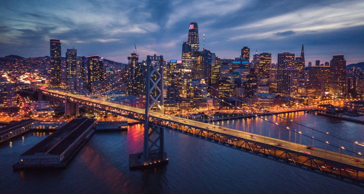 The image depicts the San Francisco skyline lit up at night with the Golden Gate Bridge in the front lit up.