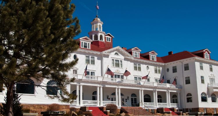 The image depicts the Stanley Hotel. It's a large white building with a a covered front porch and red roof.
