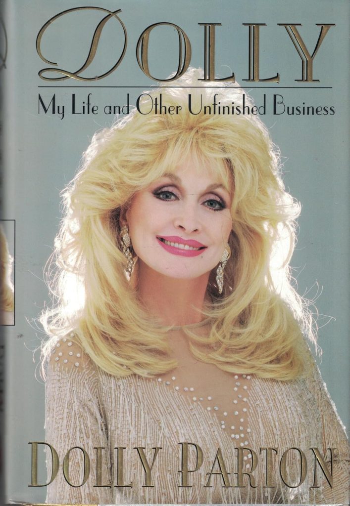 Dolly: My Life and Other Unfinished Business by Dolly Parton book cover. Depicts Dolly Parton smiling with big blonde hair, a white sparkling dress, and large sparkling earrings.