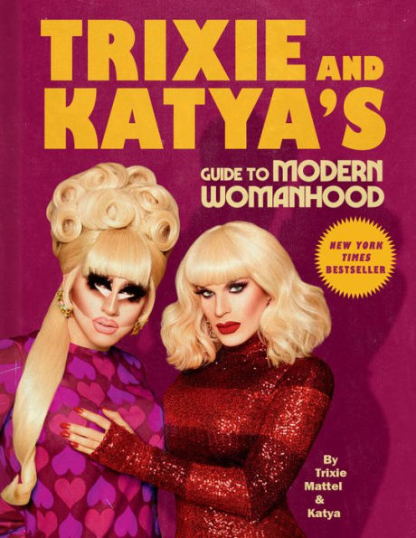 Book cover features two drag queens with glamorous blonde wigs and bold makeup, set against a purple background. Text reads “Trixie and Katya’s Guide to Modern Womanhood,” labeled as a New York Times Bestseller.