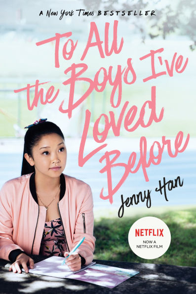 Book cover of "To All the Boys I've Loved Before" by Jenny Han. Young woman sits at a table outdoors, wearing a pink jacket, writing in a notebook.