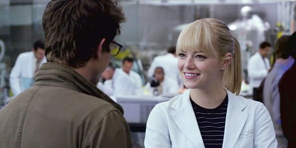 The Amazing Spider-Man 2 still depicts Gwen Stacy smiling at Peter Parker with her hair in a ponytail and a white lab coat on. Behind them, there are a lot of people wearing white lab coats.