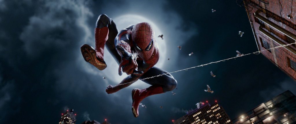 The Amazing Spider-Man still depicts Spider-Man hanging from a web and shooting a web downwards towards the camera. The background shows a white, full moon, pigeons, and buildings towards the bottom of the image.