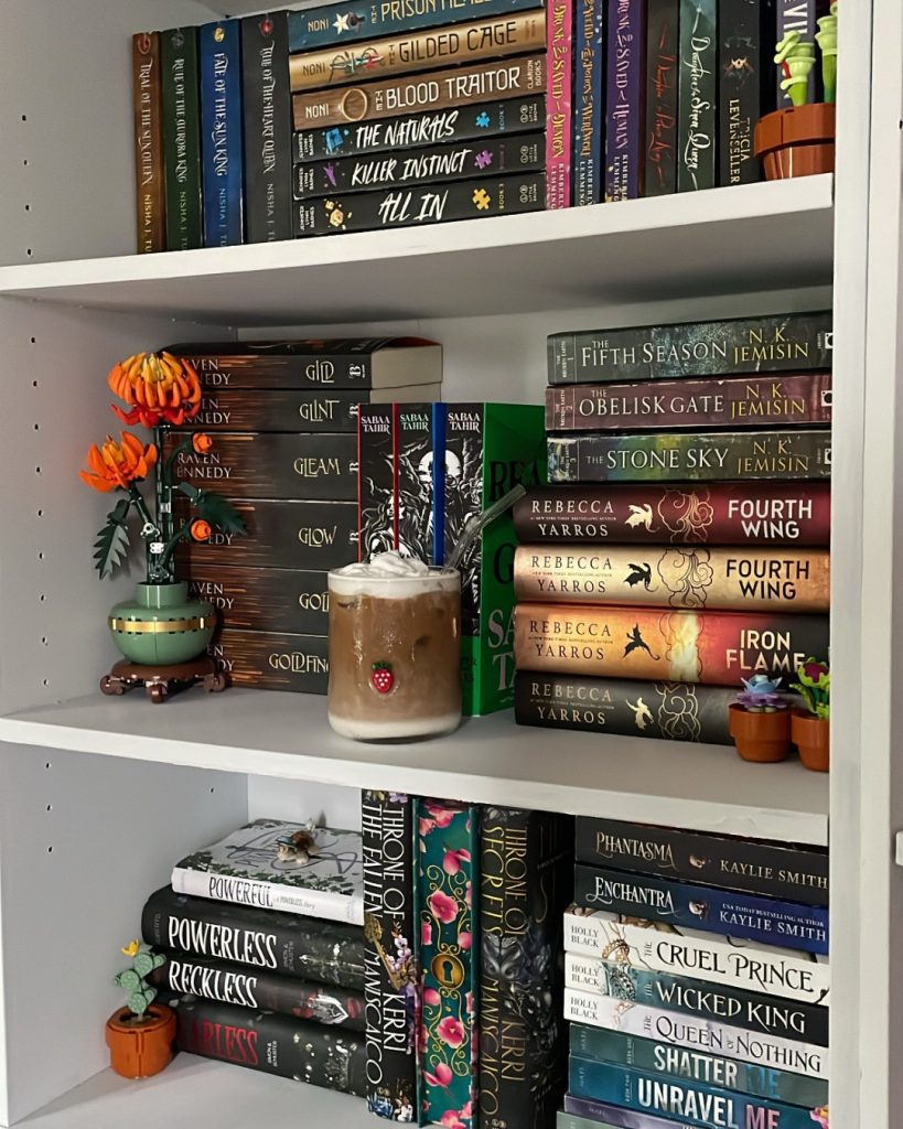 A white bookshelf stacked with books. There are three shelves in the frame, each decorated with one or more decorative pots with fake plants.