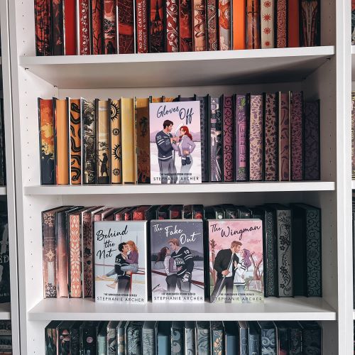 A white bookcase with books arranged spines in, the pages color-coordinated. Displayed on the second shelf is a copy of Gloves Off by Stephanie Archer, and displayed on the third shelf are copies of Behind the Net, The Fake Out, and The Wingman, all by Stephanie Archer.