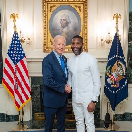 Mayor Randall Woodfin and President Joe Biden shaking hands at the white house between two flags with a portrait of George Washington in the background.