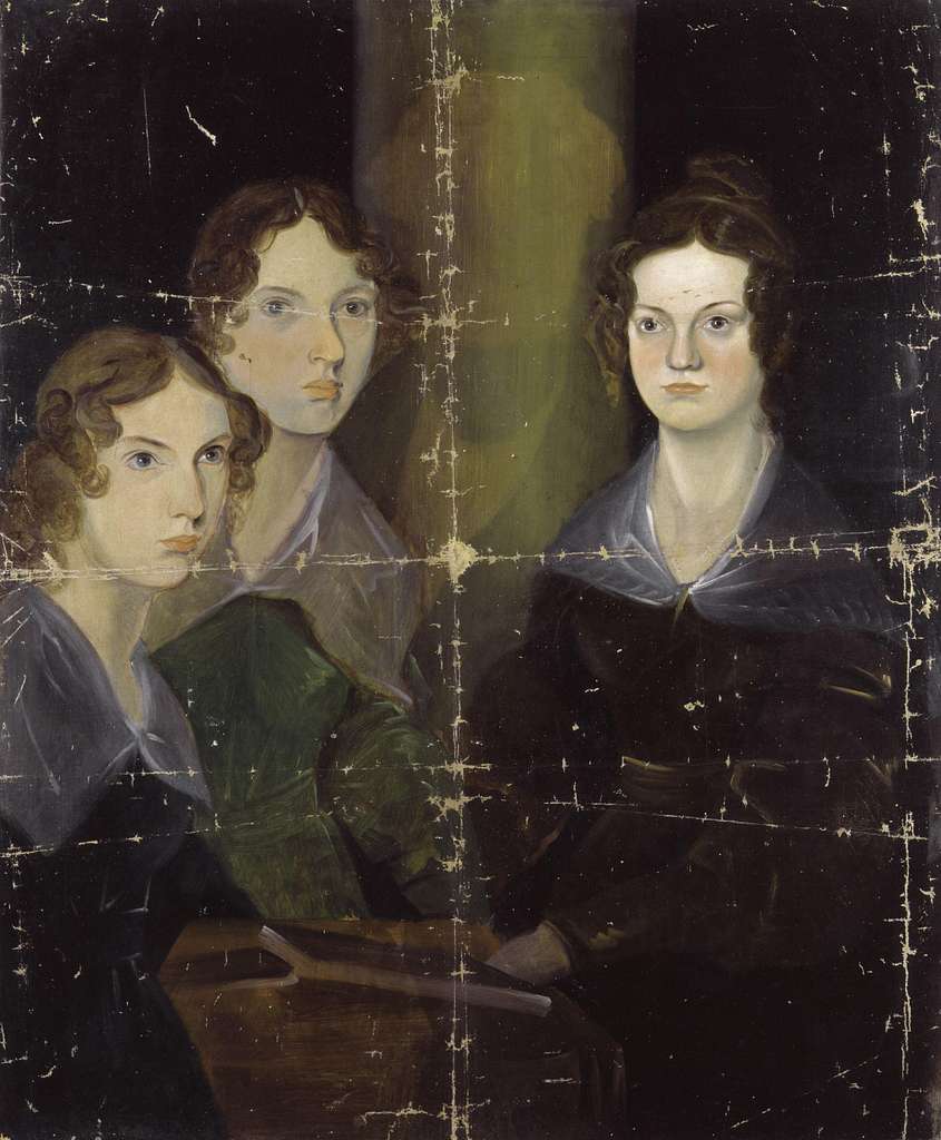 Portrait of the three Bronte sisters. On the far left is Anne wearing a dark dress with a grey collar, her light brown hair in curls around her face. In the middle is Emily, with darker brown hair and a similar collared dress in a green style. On the far right is charlotte, wearing a dark brown, dark grey collared dress. Her dark brown hair is styled in ringlets around her face, with the rest in a updo at the back of her head. They sit posed around a small wooden desk with a book in front of each of them. The background is black with the exception of a yellowish-brown shadow between Emily and Charlotte.
