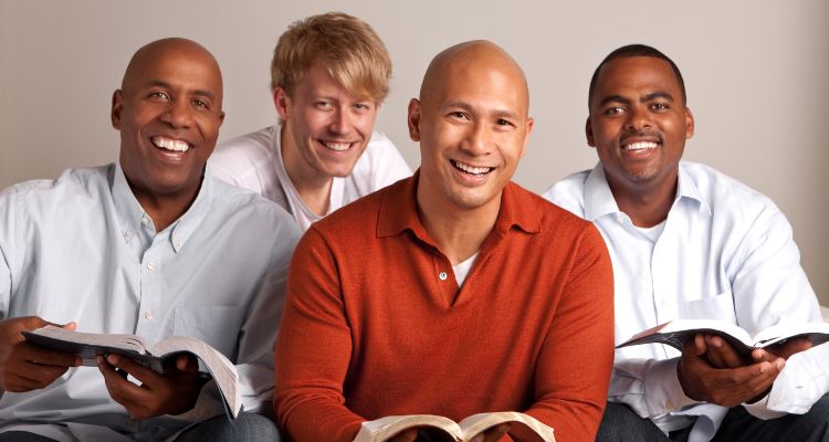 Four ethnically diverse men smiling while holding open books on a gray background.
