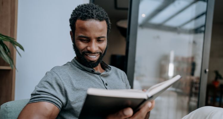 A Black man smiling and reading a book.