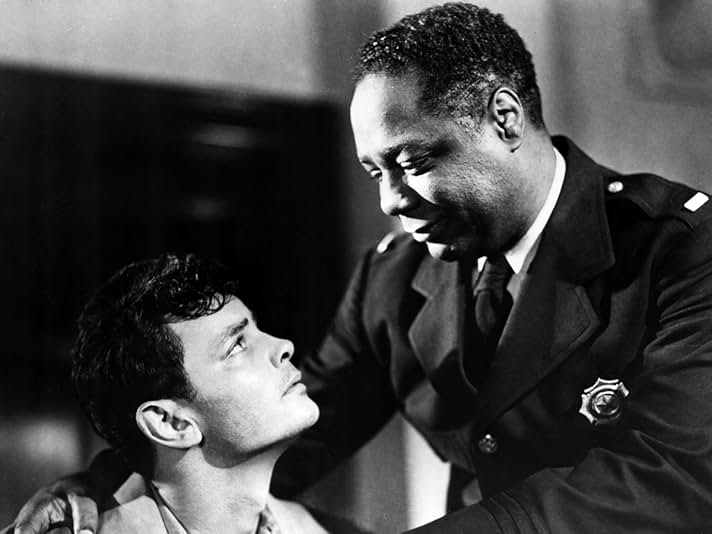 A still from the 1949 film Lost Boundaries. A White man looks up at a Black uniformed police officer. The Black man smiles.