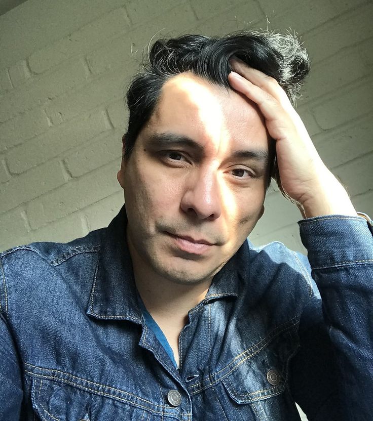 Image of author Manuel Muñoz. A middle-aged man with short, black hair is wearing a denim jacket with his hand in his hair.