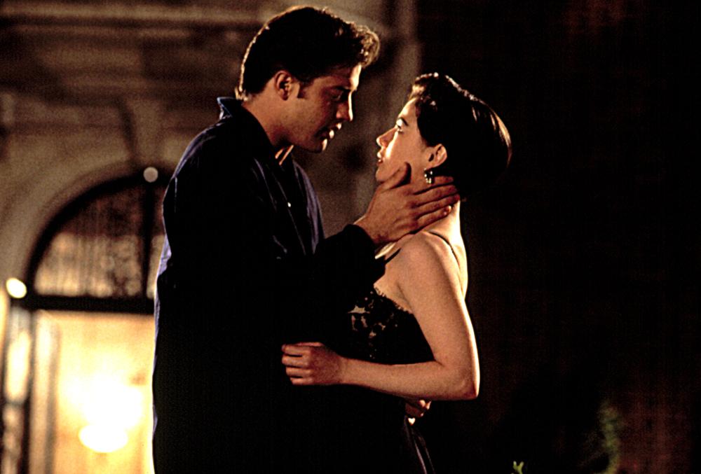 A still from With Honors. A young man wearing a dark blue pajama set holds a young woman in a black lacy nightgown as if he is about to kiss her.