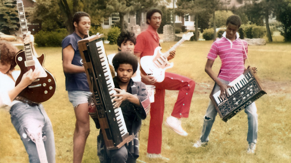 Move Ya Body: The Birth of House film still. A group of musicians play their instruments standing on a lawn in front of a house.