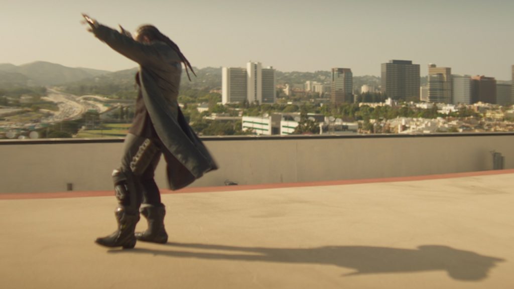 Still Free TC film still. Ty Dolla $ign stands on an empty concrete roof with his hands raised and a cityscape behind him.