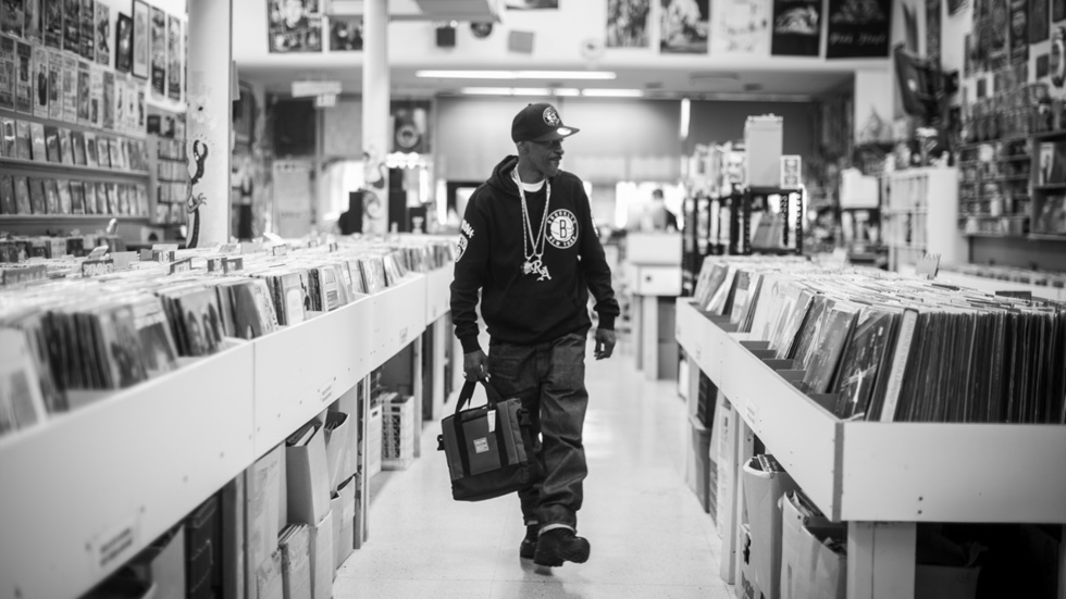 The Sixth Borough film still. A black and white image of a man browsing a record store and holding a record carrying bag.