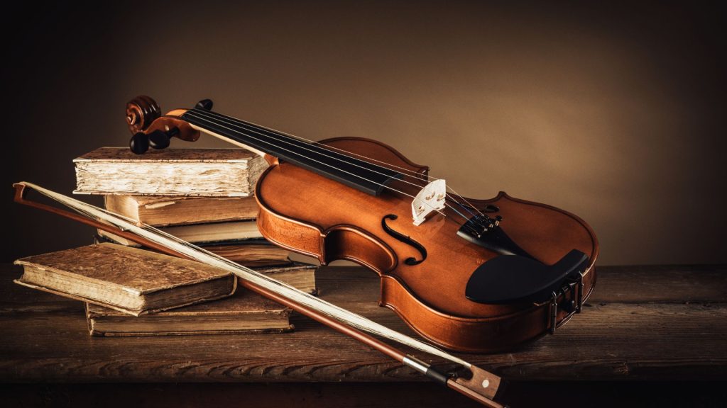 Violin and bow lean on a stack of books on a hardwood surface with a brown background.