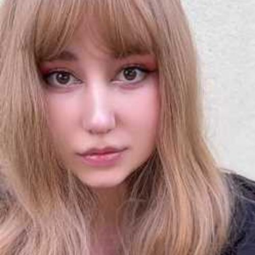 Headshot of Veronica Lancet. She is pale-skinned, has blonde hair and bangs, and is wearing eyeliner and pink lip gloss. The background is white.