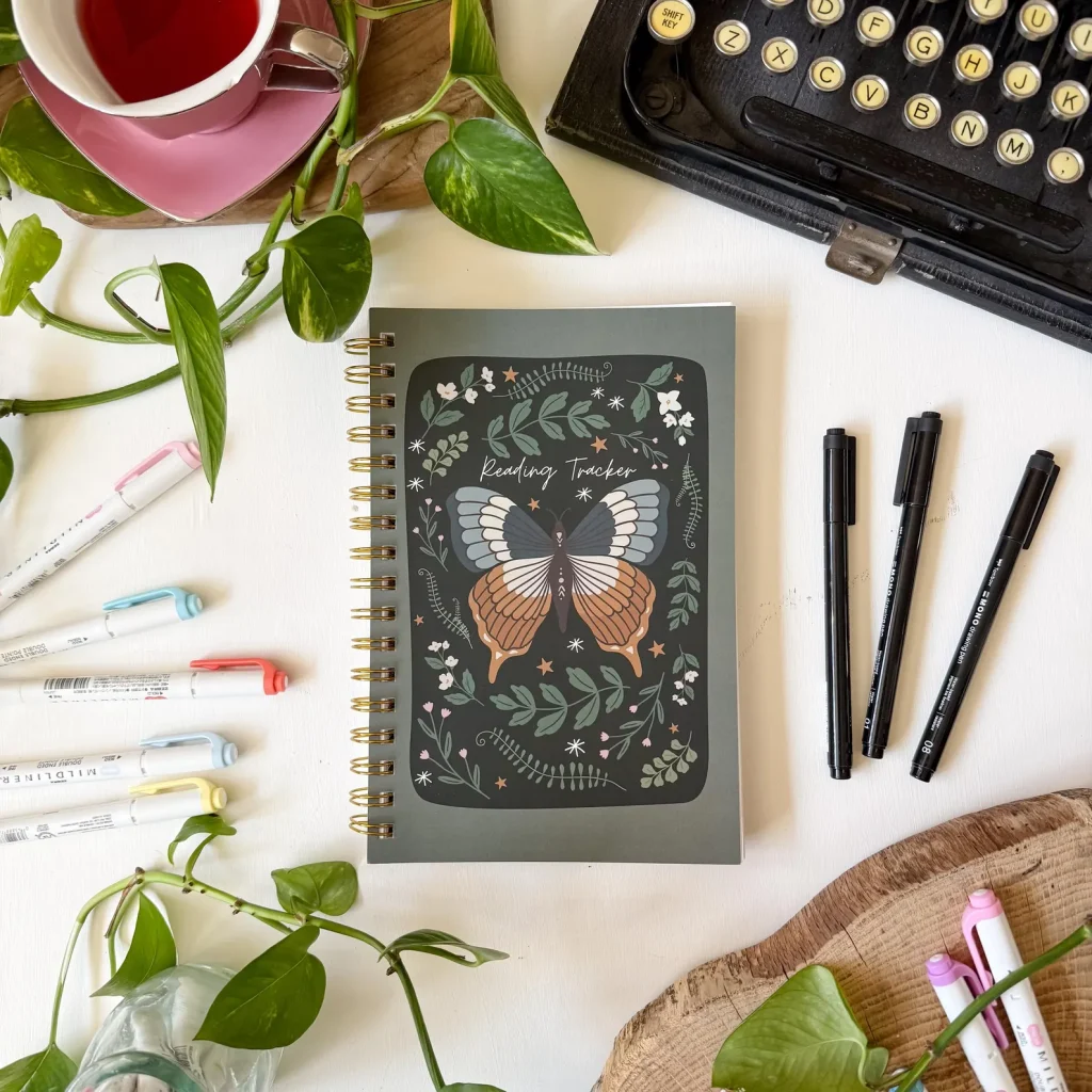 A dark green journal with a moth in the center and floral patterns surrounding it. The words Reading Journal in white cursive above the moth.