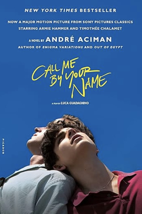 Call Me By Your Name by André Aciman. Shows two young men leaning against each other under a vivid blue sky, with bold yellow handwritten-style title text above them.