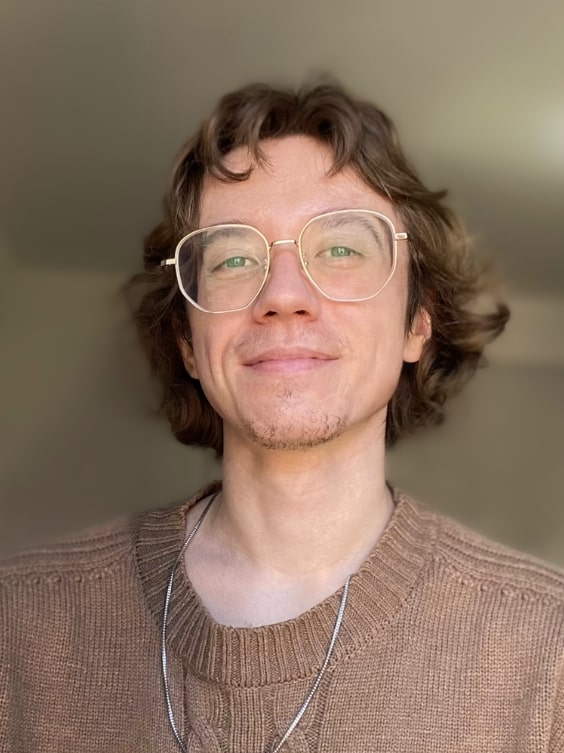 Author Page Powars in gold rimmed glasses and a brown sweater smiling at the camera