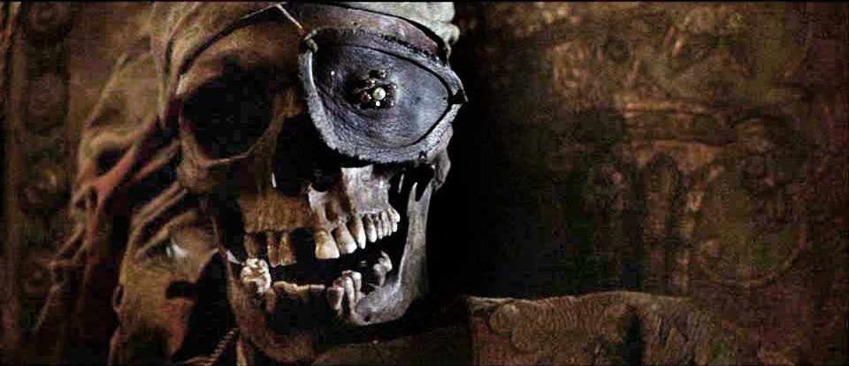 A still from the 1985 movie The Goonies. A skull wearing a black eyepatch and brown bandana leans against a brown upholstered chair.