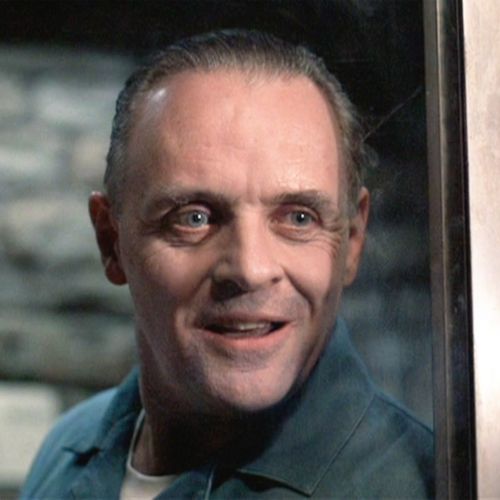 Horror Character Hannibal Lector, a white man with blue eyes smiling, wearing a black jacket with a white top underneath.
